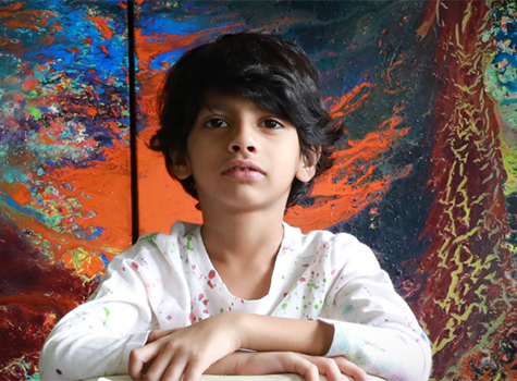 A young boy sitting in front of an abstract painting.